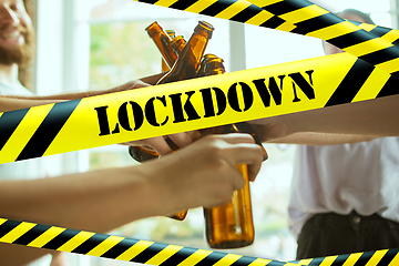 Image showing Close up hands clinking bottles of beer at bar with bounding tapes Lockdown, Coronavirus, Quarantine, Warning - closing bars and nightclubs during pandemic