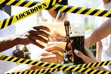 Image showing Close up hands clinking glasses of beer at bar with bounding tapes Lockdown, Coronavirus, Quarantine, Warning - closing bars and nightclubs during pandemic