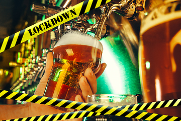 Image showing Hand of bartender pouring a beer in tap with bounding tapes Lockdown, Coronavirus, Quarantine, Warning - closing bars and nightclubs during pandemic