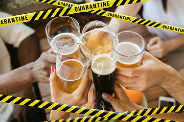 Image showing Close up hands clinking glasses of beer at bar with bounding tapes Lockdown, Coronavirus, Quarantine, Warning - closing bars and nightclubs during pandemic