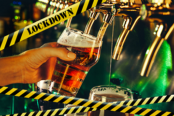 Image showing Hand of bartender pouring a beer in tap with bounding tapes Lockdown, Coronavirus, Quarantine, Warning - closing bars and nightclubs during pandemic