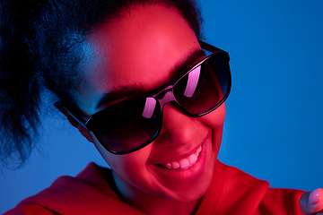 Image showing African-american woman\'s portrait isolated on blue studio background in multicolored neon light