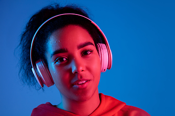 Image showing African-american woman\'s portrait isolated on blue studio background in multicolored neon light