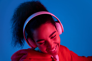 Image showing African-american woman\'s portrait isolated on blue studio background in multicolored neon light