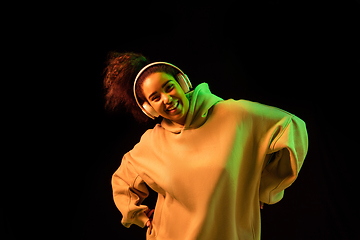 Image showing African-american woman\'s portrait isolated on dark studio background in orange-green neon light