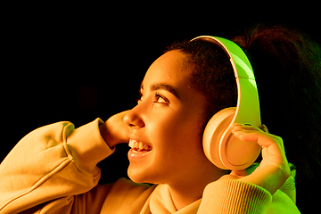 Image showing African-american woman\'s portrait isolated on dark studio background in orange-green neon light