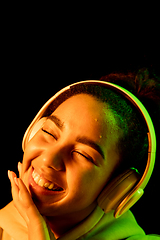 Image showing African-american woman\'s portrait isolated on dark studio background in orange-green neon light