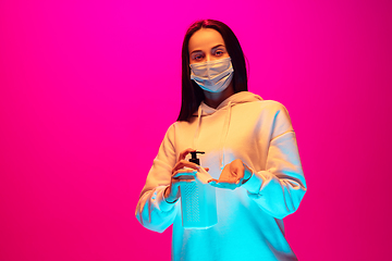 Image showing Caucasian beautiful woman\'s portrait isolated on pink studio background in multicolored neon light. Wearing face mask.