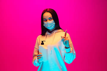 Image showing Caucasian beautiful woman\'s portrait isolated on pink studio background in multicolored neon light. Wearing face mask.