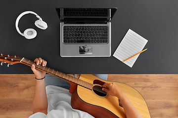 Image showing young man with laptop playing guitar at table