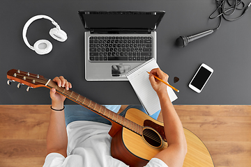 Image showing man with guitar writing to music book at table