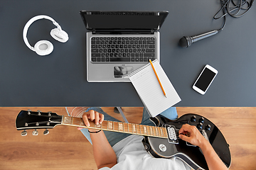 Image showing young man with laptop playing guitar at table