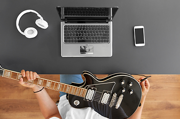 Image showing young man with laptop tuning guitar at table