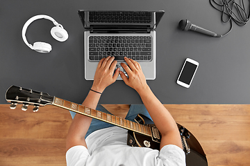 Image showing young man with laptop and guitar at table