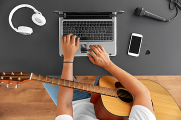 Image showing young man with laptop playing guitar at table