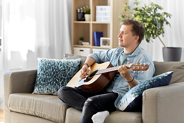 Image showing young man playing guitar sitting on sofa at home