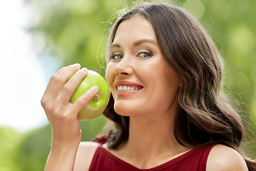 Image showing happy woman eating green apple at summer park