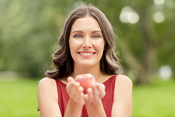 Image showing happy woman eating peach at summer park