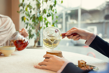 Image showing Close up female hands pouring tea in cup at restaurant or cafe, daily lifestyle