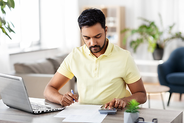 Image showing man with calculator and papers working at home