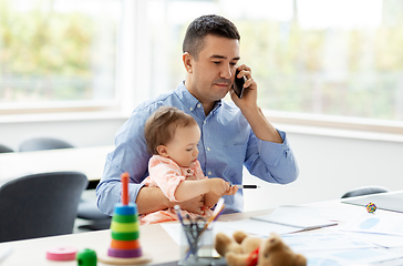 Image showing father with baby calling on phone at home office