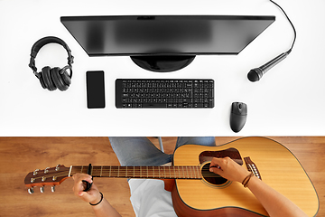 Image showing young man with computer playing guitar at table