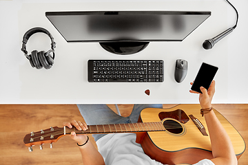 Image showing young man with guitar and smartphone at table