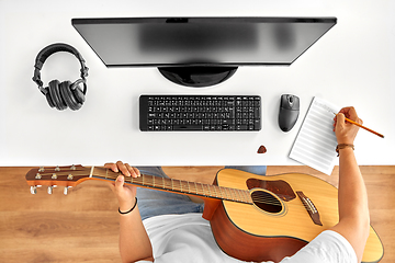 Image showing man with guitar writing to music book at table