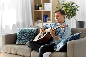 Image showing young man playing guitar sitting on sofa at home