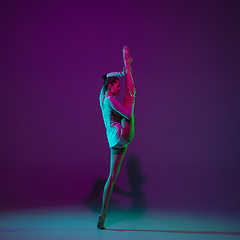 Image showing Young female athlete, rhythmic gymnastics artist on purple background with neon light. Beautiful girl practicing with equipment. Grace in performance.