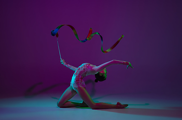 Image showing Young female athlete, rhythmic gymnastics artist on purple background with neon light. Beautiful girl practicing with equipment. Grace in performance.