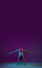 Image showing Young female athlete, rhythmic gymnastics artist on purple background with neon light. Beautiful girl practicing with equipment. Grace in performance.