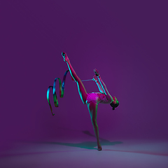 Image showing Young female athlete, rhythmic gymnastics artist on purple background with neon light. Beautiful girl practicing with equipment. Grace in performance.