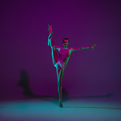 Image showing Young female athlete, rhythmic gymnastics artist on purple background with neon light. Beautiful girl practicing with equipment. Grace in performance.