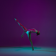 Image showing Young female athlete, rhythmic gymnastics artist on purple background with neon light. Beautiful girl practicing with equipment. Grace in performance.