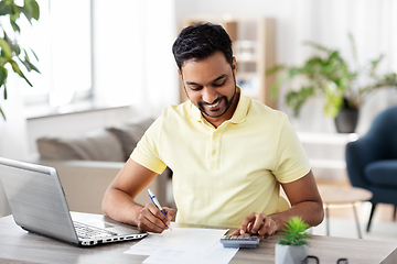 Image showing man with calculator and papers working at home