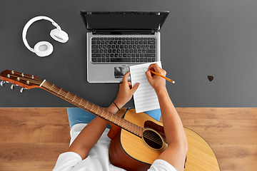 Image showing man with guitar writing to music book at table