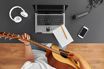 Image showing young man with laptop playing guitar at table