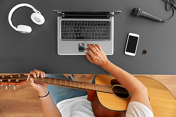 Image showing young man with laptop playing guitar at table