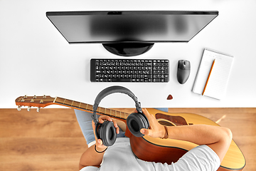 Image showing young man with headphones and guitar at table