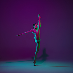 Image showing Young female athlete, rhythmic gymnastics artist on purple background with neon light. Beautiful girl practicing with equipment. Grace in performance.