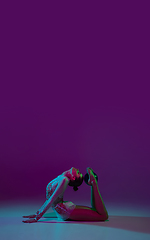 Image showing Young female athlete, rhythmic gymnastics artist on purple background with neon light. Beautiful girl practicing with equipment. Grace in performance.