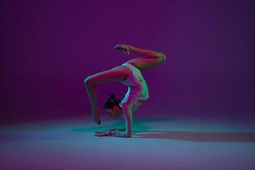 Image showing Young female athlete, rhythmic gymnastics artist on purple background with neon light. Beautiful girl practicing with equipment. Grace in performance.