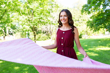 Image showing happy woman spreading picnic blanket at park