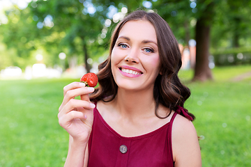 Image showing happy woman eating strawberry at summer park