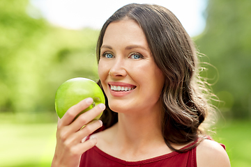 Image showing happy woman eating green apple at summer park