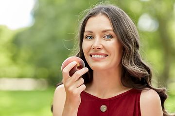 Image showing happy woman eating peach at summer park