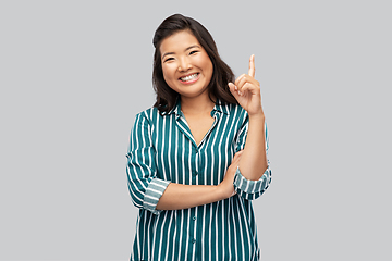 Image showing happy asian woman pointing finger up on grey