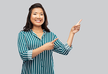 Image showing happy asian woman pointing fingers up on grey