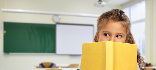 Image showing little girl hiding behind yellow book at school